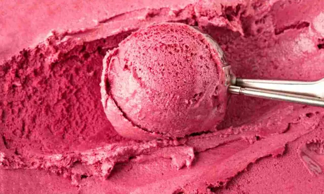 Un cucchiaio raccoglie una porzione di cremoso gelato fatto in casa, dal colore rosa intenso, su uno sfondo dello stesso dolce freddo.