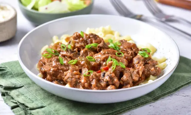 Pyszny strogonow z wieprzowiny z pieczarkami i ogórkiem kiszonym, podany z makaronem. Idealny przepis na obiad.