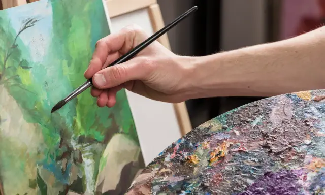Main d'artiste appliquant la peinture sur une toile, palette colorée à proximité. Une belle technique de peinture en cours.