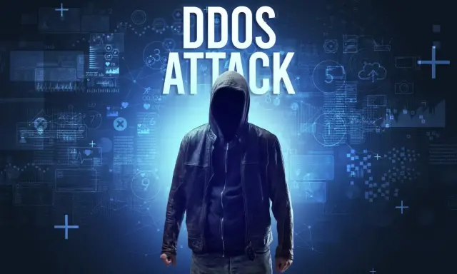 Anonimowa postać w kapturze na tle cyfrowych danych. Wielki napis "DDOS ATTACK" wyjaśnia, ddos co to.