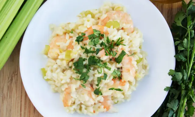Pyszne risotto z krewetkami, udekorowane natką pietruszki, obok łodygi selera i oliwy.