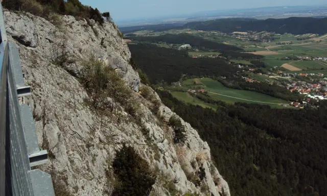 Widok z **Hohe Wand** na dolinę z lasami i wioskami. Stroma, skalista ściana po lewej stronie.