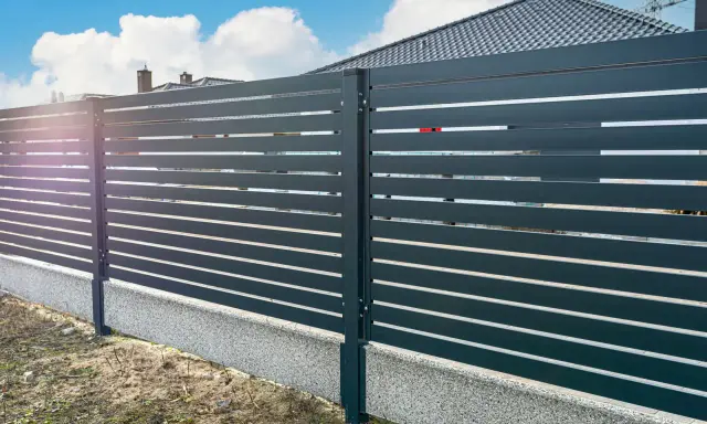 Nowoczesne ogrodzenie z poziomych paneli, osadzone na betonowym cokole. To świetne rozwiązanie co zamiast podmurówki pod ogrodzenie, zapewniające estetykę i trwałość.
