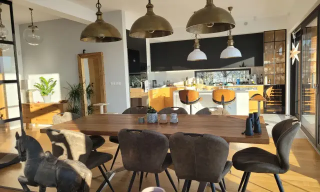 Oświetlenie salonu inspiracje: industrialne lampy wiszące nad drewnianym stołem, nowoczesna kuchnia w tle.