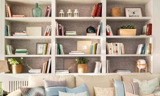 Estanterías blancas llenas de libros, plantas y objetos decorativos. Una idea de **qué poner detrás del sofá** para crear un rincón acogedor y lleno de estilo.