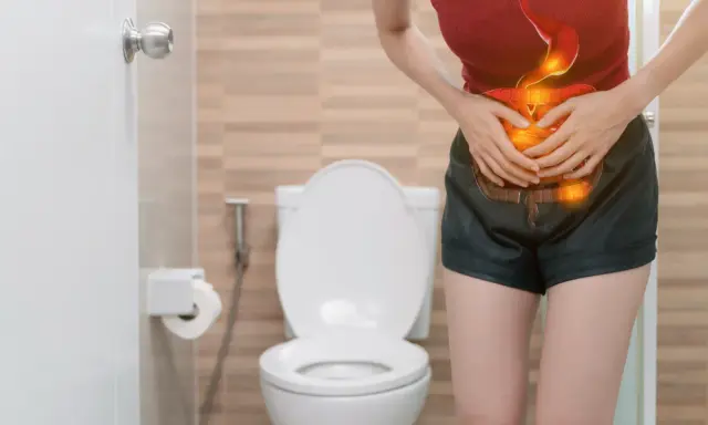 Mujer con dolor abdominal, con ilustración del sistema digestivo en rojo y naranja, frente a un inodoro.