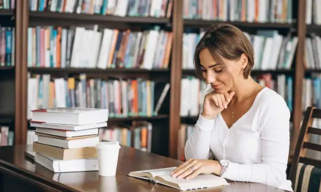 Donna legge in biblioteca, circondata da libri. Il suo studio è un esempio di come l'asindeto, nel significato e negli esempi, arricchisca la narrazione.