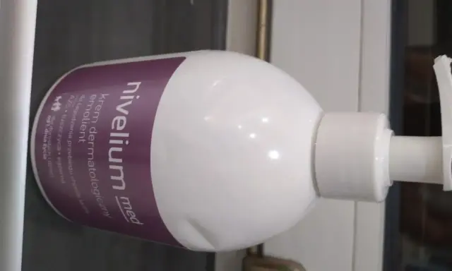 Biała butelka z pompką, na której widnieje napis "nivelium med krem dermatologiczny emolient". Idealny dla skóry z AZS i łuszczycą.