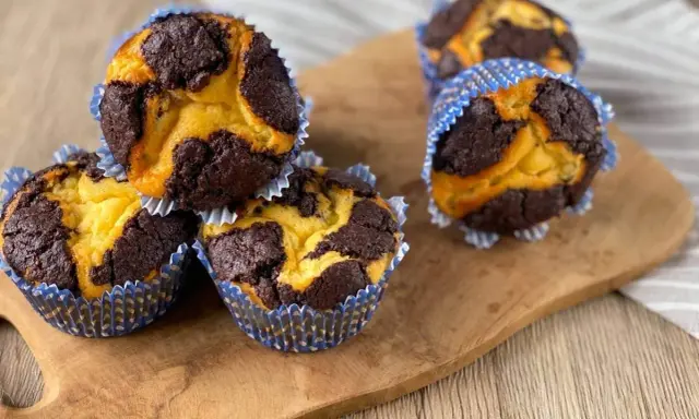 Schokoladen-Vanille-Zupfkuchen-Muffins in blauen Papierförmchen auf einem Holzbrett.