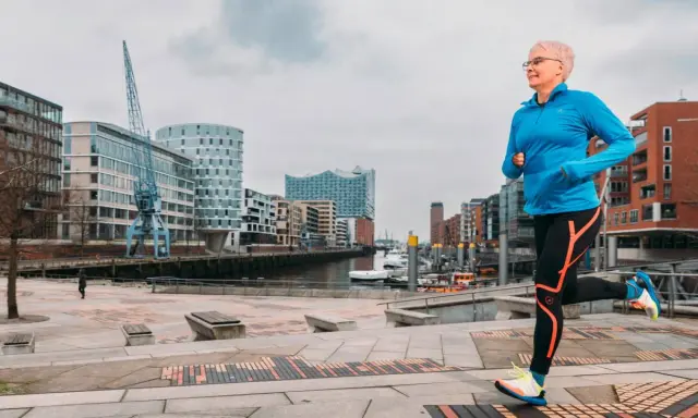 Frau mit kurzen Haaren läuft im Hafen. Sie trägt Sportkleidung und Schuhe. Mit Laufen abnehmen ist ihr Ziel.
