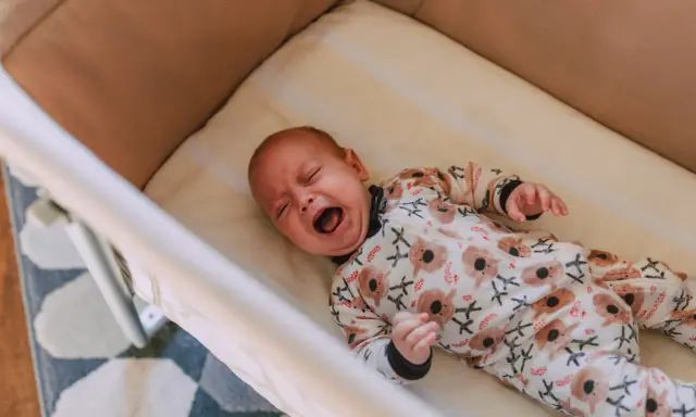 Bebé llorando en su cuna, con un pijama de koalas. Un momento difícil para dejar llorar a un niño de 2 años para dormir.