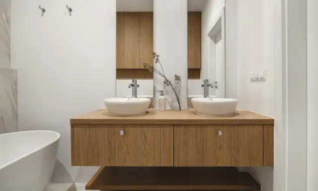 Nowoczesna łazienka z dwoma umywalkami na drewnianej szafce. Minimalistyczny design, białe ceramika i ciepłe drewno tworzą harmonijną przestrzeń.