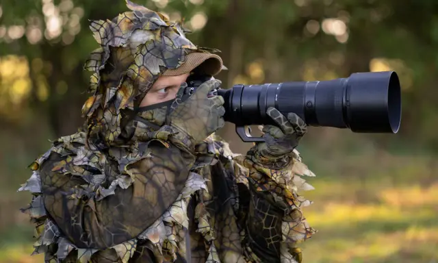 Fotograf w ghillie suit z aparatem do fotografowania zwierząt czeka na idealny kadr.