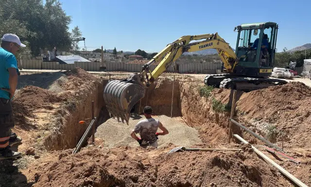 Excavadora amarilla trabajando para cavar zanjas en un día soleado. Un hombre supervisa la obra.