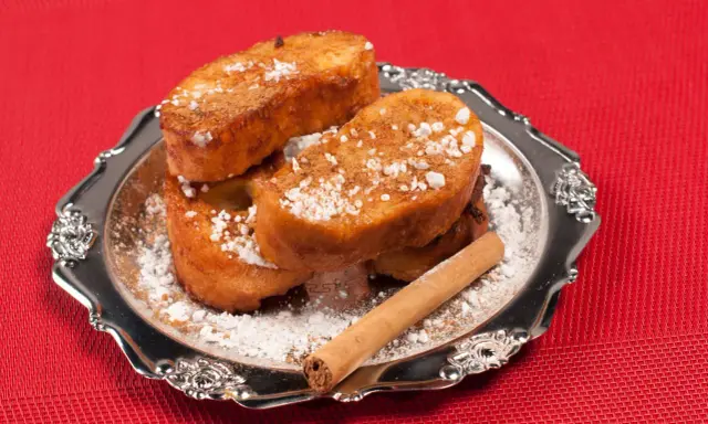 Torrijas de Semana Santa espolvoreadas con azúcar glas y canela, servidas en un plato plateado con una rama de canela.