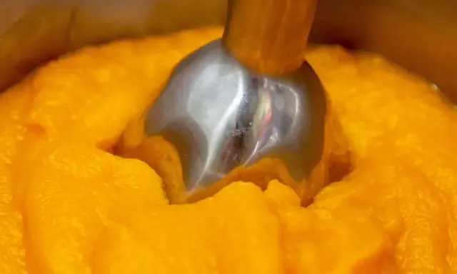 Metalowa końcówka blendera zanurzona w gęstym, pomarańczowym puree z dyni.