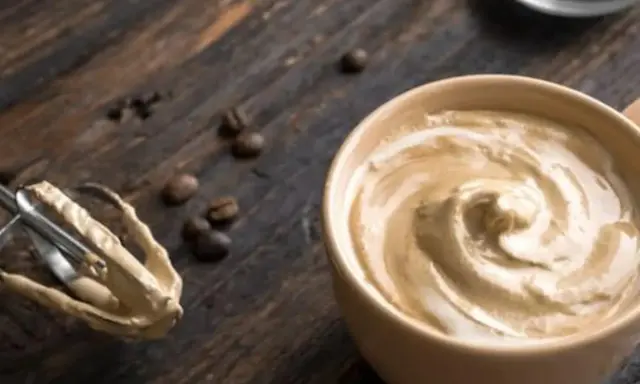 Cremige Crema al Caffè in einer Tasse, daneben ein Handmixer mit Teigresten und Kaffeebohnen auf Holz.