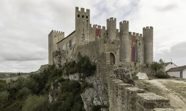 Die Obidos Burg thront majestätisch auf einem Felsen. Fahnen mit dem Namen "Obidos" wehen im Wind.