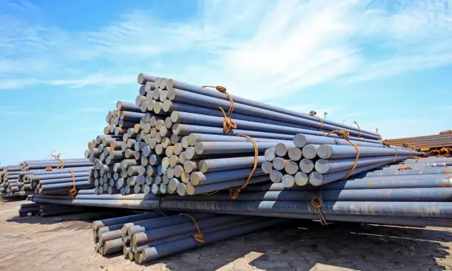 Stapel von Metallstäben, die den Unterschied zwischen Eisen und Stahl veranschaulichen. Sie liegen unter blauem Himmel.
