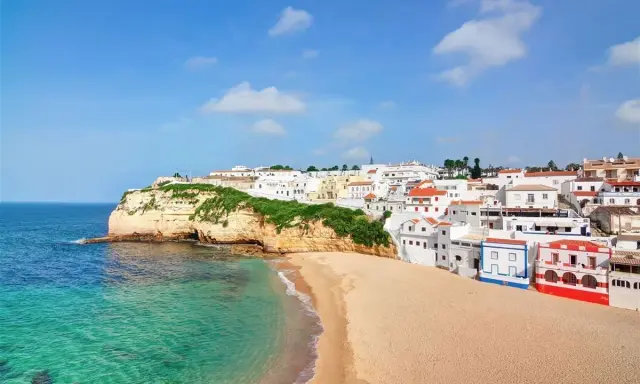 Traumhafte Küstenlandschaft in Portugal, Carvoeiro: Weiße Häuser schmiegen sich an grüne Klippen, daneben ein goldener Sandstrand und türkisfarbenes Meer.