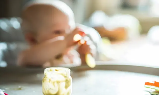 Słoiczek z puree ziemniaczanym, idealny do nauki, jak przygotować ziemniaka dla niemowlaka. W tle widać dziecko.