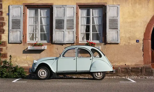 Jasnoniebieski, zabytkowy Citroen 2CV, jeden z tych klasycznych, francuskich modele stare, stoi przed kamiennym domem z drewnianymi okiennicami.