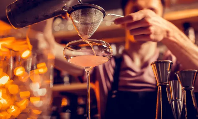 Un barman verse un cocktail d'un shaker dans un verre. C'est ainsi qu'un shaker sert à mélanger et refroidir les boissons.