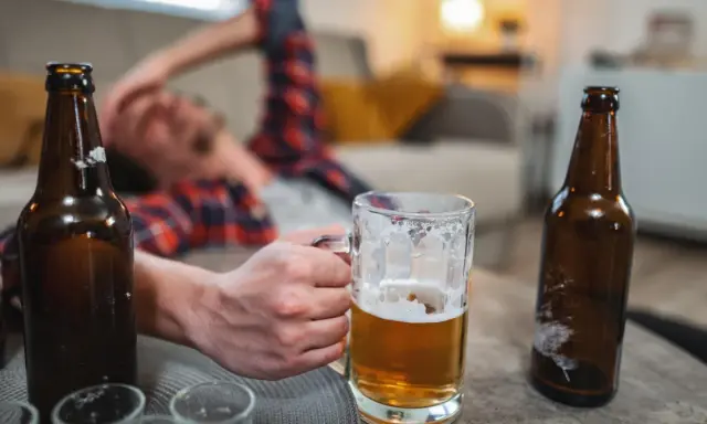 Mężczyzna leży na kanapie, trzymając kufel piwa. Wokół leżą puste butelki. Czy to oznacza, co przyspiesza spalanie alkoholu?