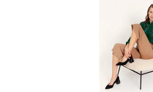Eleganckie czarne czółenka na geometrycznym obcasie to idealne buty na jesień. Modelka prezentuje je w stylizacji z beżowymi spodniami i zieloną bluzką.