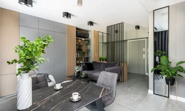 Nowoczesne mieszkanie 30m2 aranżacja: szara sofa, marmurowy stół, dużo zieleni i lustro.