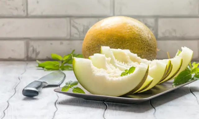 Kawałki melona na talerzu, obok cały owoc i nóż. Niska wartość melon indeks glikemiczny.