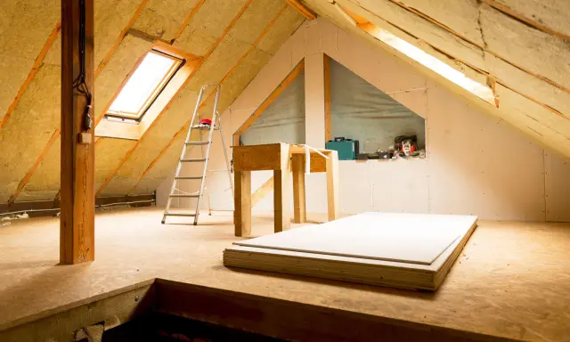 Un grenier en cours d'aménagement, avec isolation, un velux, une échelle et des plaques de plâtre.