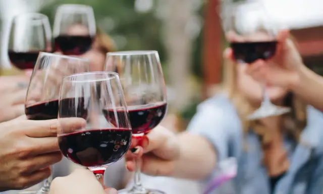 Des mains portent des verres de vin rouge pour un apéro convivial.