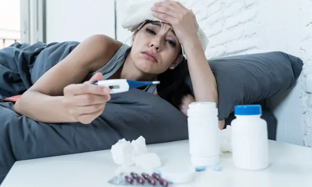 Donna malata a letto con termometro e medicine, preoccupata per i ciproxin effetti collaterali.