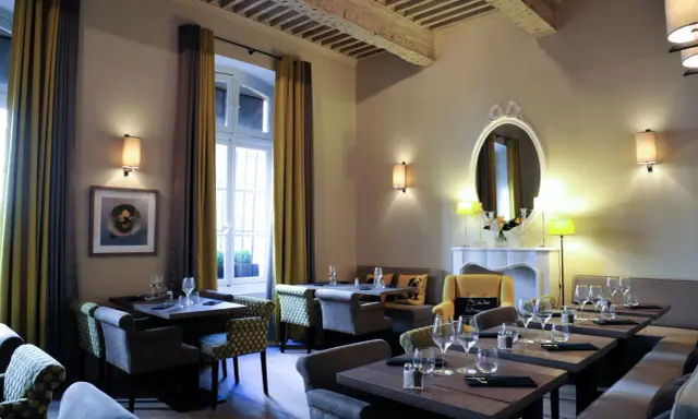 Salle à manger élégante avec tables dressées, fauteuils confortables et un miroir orné. L'ambiance évoque une **spécialité provençale** raffinée.