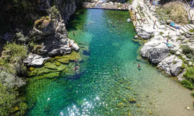 Una espectacular piscina natural en Extremadura, con aguas cristalinas y gente disfrutando del baño entre rocas y vegetación.