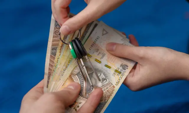 Dwie ręce trzymają plik banknotów i klucze. Zastanawiasz się, od jakiej kwoty płaci się podatek od wynajmu mieszkania?
