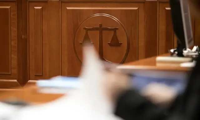 Drewniana ściana z symbolem wagi sprawiedliwości. Zastanawiasz się, ile czeka się na rozprawę w sądzie cywilnym? Czas oczekiwania bywa długi.