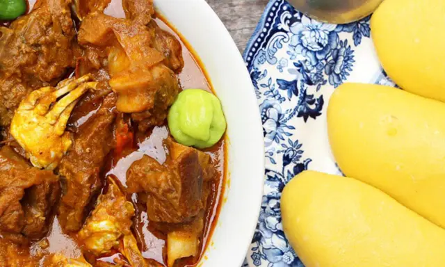 Un plat de foutou sauce graine avec de la viande et du crabe, accompagné de boules de pâte jaune sur une assiette décorée.