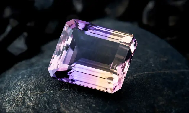 Un taglio a smeraldo sfaccettato mostra la transizione tra ametista e quarzo rosa, un connubio di colori su una roccia scura.