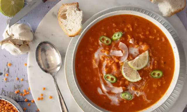 Eine cremige rote Linsensuppe mit Kokosmilch, garniert mit Limettenspalten und Jalapeños. Dazu gibt es knuspriges Brot.