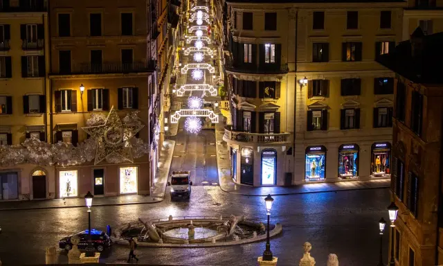 Roma di notte a Natale: una strada illuminata da luci scintillanti, negozi di lusso e una fontana. Un'atmosfera magica per scoprire cosa vedere a Roma a Natale.