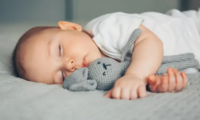 Ein Baby schläft friedlich mit seinem Häschen-Spielzeug. Vielleicht ist es die berüchtigte 4 monats schlafregression, die es so müde macht.