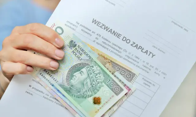 Dłoń trzyma wezwanie do zapłaty i polskie banknoty 100 i 200 zł. Dokument zawiera informację o zawiadomieniu o uchyleniu zajęcia.