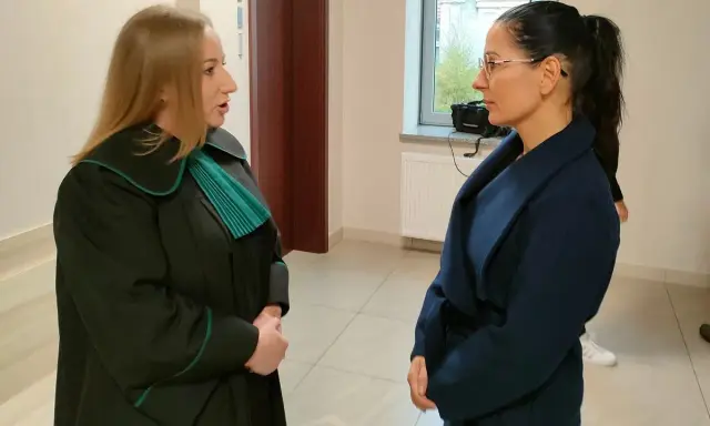 Prawniczka w todze rozmawia z kobietą w granatowym płaszczu.