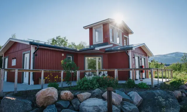 Rött hus med vita knutar och en solig veranda. Abisko Turiststation välkomnar besökare till fjällen.