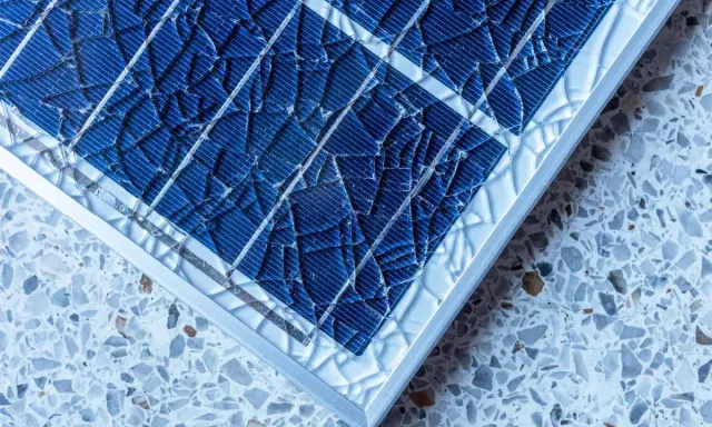 Gros plan sur un vitre panneau solaire brisé, ses fragments bleus reflétant la lumière sur un fond moucheté.