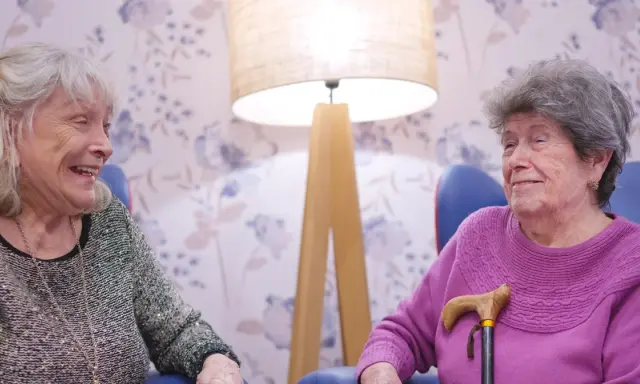 Dwie starsze panie rozmawiają, śmiejąc się. Ich uśmiechy sugerują, że znają sekret, jak utrzymać związek.