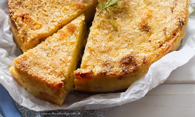 Delizioso gateau di patate dorato e croccante, guarnito con rosmarino fresco. Una fetta è già stata tagliata, invitando ad assaporare questo piatto saporito.