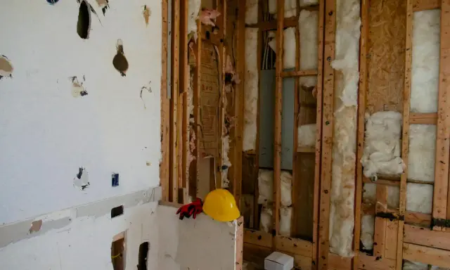 Chantier en cours, murs ouverts révélant l'isolant. Attention, la laine de bois peut présenter un danger si mal manipulée. Casque et gants de protection à proximité.